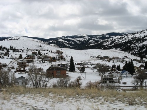 A snowy landscape with a small town nestled in the mountains, under a cloudy sky.