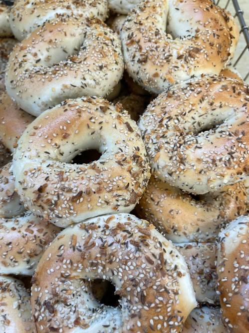 A close-up of freshly baked bagels topped with sesame and poppy seeds, piled together in a basket.
