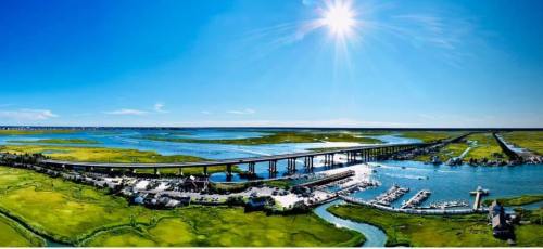 A panoramic view of a bridge over a river, surrounded by lush greenery and a bright blue sky.