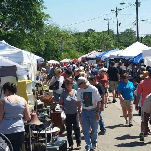 A bustling outdoor market with numerous tents, vendors, and a crowd of people browsing various goods.