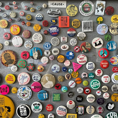 A collage of colorful buttons and pins with various slogans and designs on a gray background.