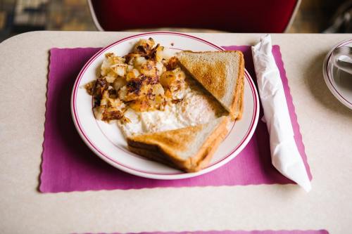 A plate with toast, scrambled eggs, and crispy hash browns on a table with a pink placemat and a napkin.