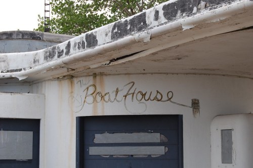 Sign reading "The Boat House" on a weathered building with peeling paint and a partially obscured door.