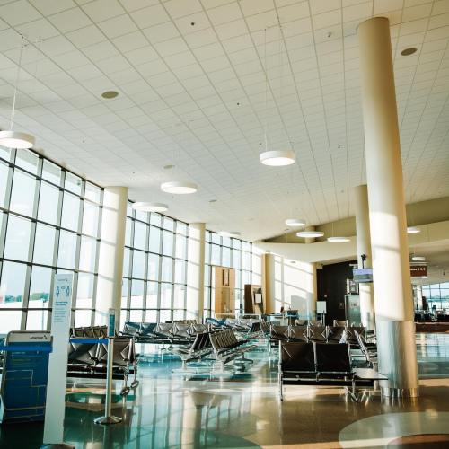 Bright, spacious airport terminal with large windows, empty seating areas, and modern lighting fixtures.