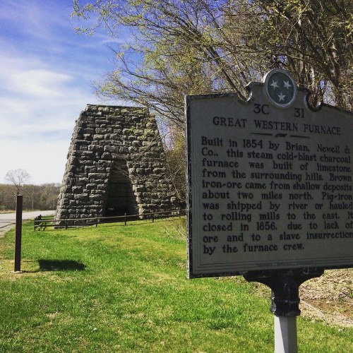 Historic stone structure with a sign about the Great Western Furnace, surrounded by trees and grassy area.