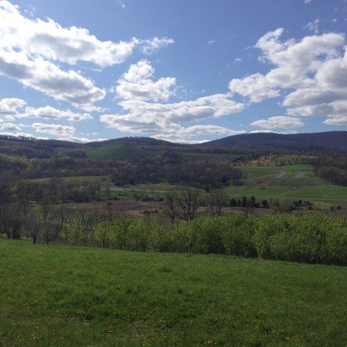 A scenic landscape featuring rolling hills, green fields, and a blue sky with fluffy clouds.