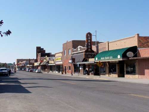 A small town street lined with shops and businesses, featuring vintage signage and clear blue skies.