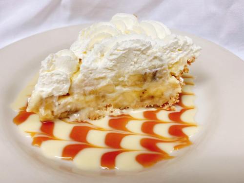A slice of banana cream pie topped with whipped cream, served on a plate with swirls of caramel and vanilla sauce.