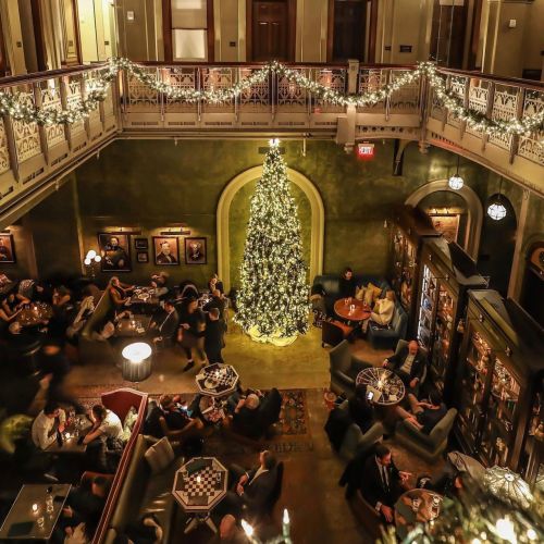 A festive restaurant interior with a large Christmas tree, dim lighting, and patrons enjoying their meals.
