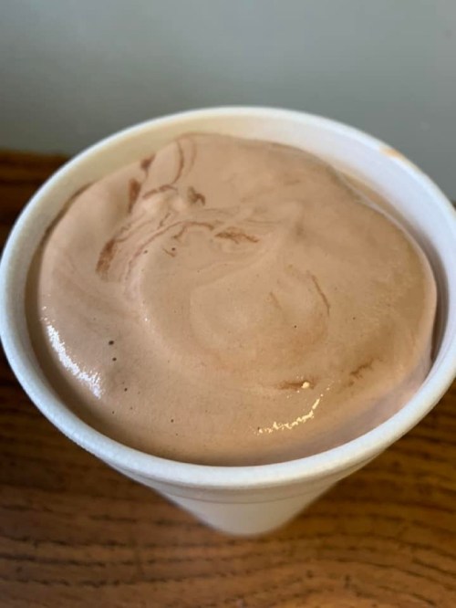 A cup filled with creamy chocolate ice cream, slightly swirled on top, resting on a wooden surface.
