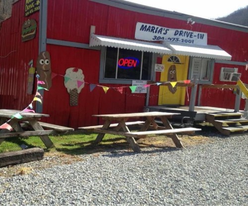 A red drive-in restaurant with picnic tables outside, an "OPEN" sign, and colorful banners. Ice cream decor is visible.