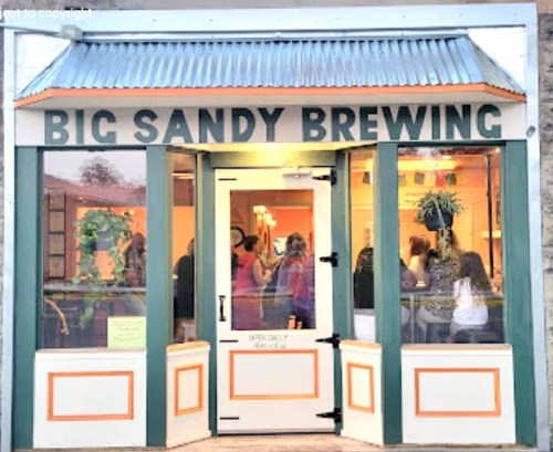 Exterior of Big Sandy Brewing, featuring large windows and a welcoming entrance with people inside.