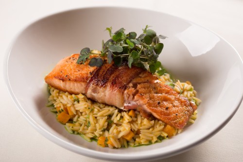 A plated dish featuring grilled salmon on a bed of orzo with herbs and vegetables.