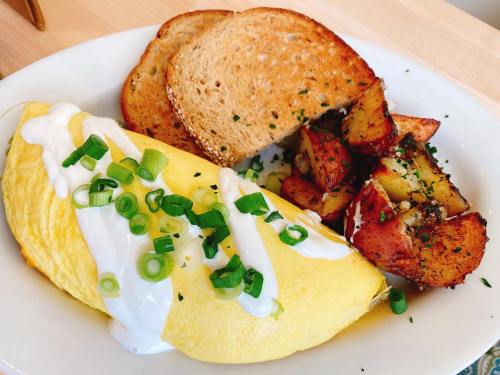 A plate with a fluffy omelette topped with green onions, served with roasted potatoes and toasted bread.
