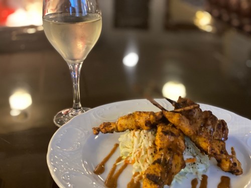 A plate of grilled chicken skewers on a bed of coleslaw, accompanied by a glass of white wine.