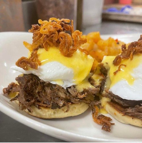 Two poached eggs on biscuits topped with shredded beef, hollandaise sauce, and crispy onions, served with diced potatoes.