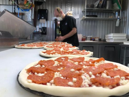 A chef prepares pepperoni pizzas in a kitchen, with several uncooked pizzas lined up on the counter.