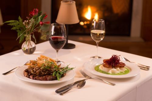 A beautifully set table with two gourmet dishes, a glass of red wine, a glass of white wine, and a small floral arrangement.