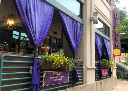 Exterior of Dizzy's restaurant featuring purple curtains and flower planters, with signage visible.