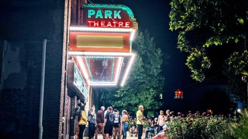 Crowd gathered outside the illuminated Park Theatre at night, with vibrant marquee lights and trees in the background.