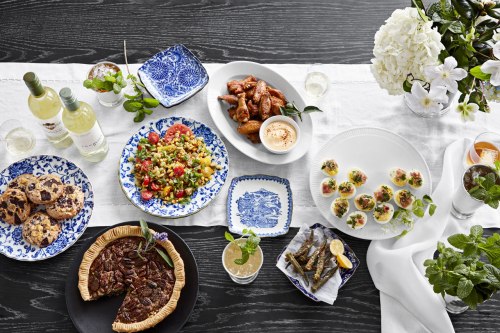 A beautifully arranged table with various dishes, including salad, wings, cookies, and a pecan pie, surrounded by flowers.