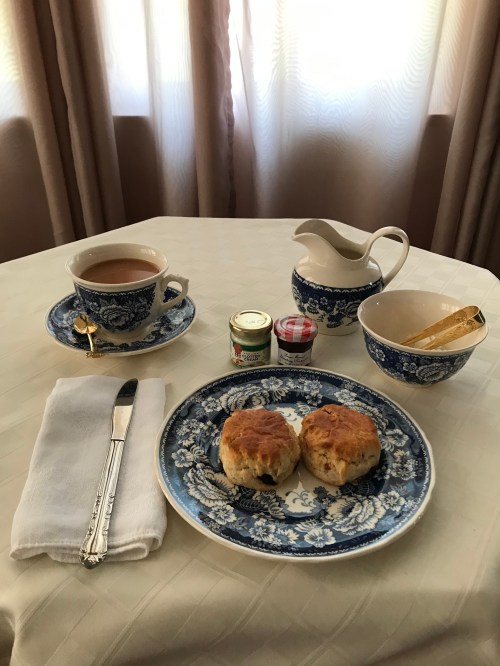 A table set with a cup of tea, scones, jam, and cream in blue floral dishes, with a white napkin and cutlery.