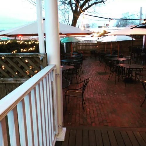 Outdoor dining area with empty tables and umbrellas, surrounded by string lights and trees, during twilight.