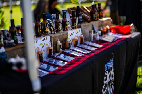 A display table featuring various bottles of sauces and condiments, with colorful labels and a black tablecloth.