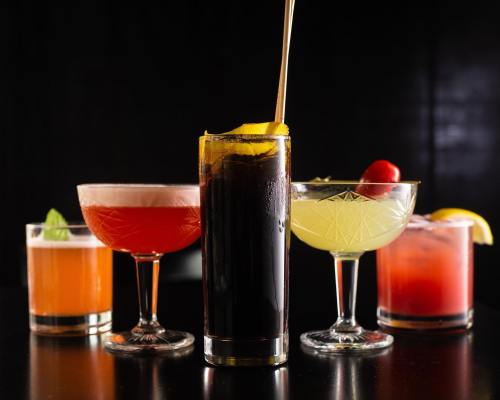 A variety of colorful cocktails in elegant glasses, featuring garnishes like lemon, cherry, and mint.