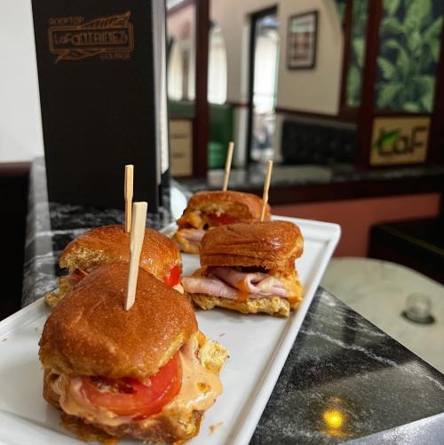 A platter of mini sandwiches with tomato and cheese, served on a white plate with toothpicks, on a marble table.