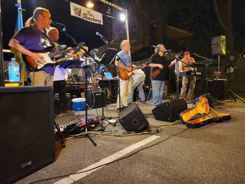 A band performs on stage at night, with musicians playing guitars and singing, surrounded by instruments and equipment.