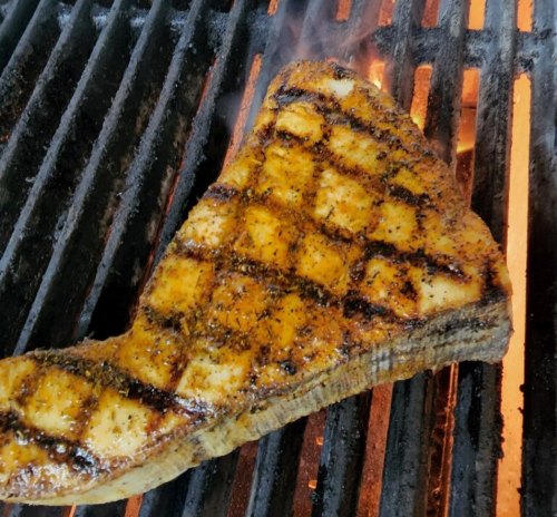 A perfectly grilled piece of fish with a crisscross sear pattern, resting on a hot grill with flames visible.