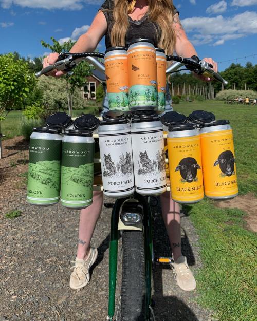 A person on a bike with various colorful beer cans attached to the front, set against a sunny outdoor backdrop.
