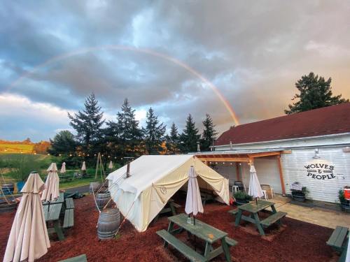 A tent and picnic tables under a rainbow, with trees and a building in the background.