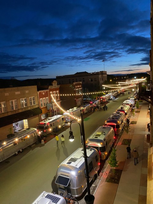 Aerial view of a street lined with vintage Airstream trailers, illuminated by string lights at dusk.