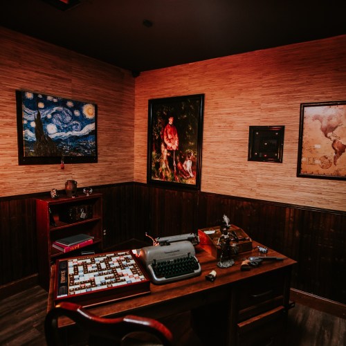 A cozy room with a wooden desk, typewriter, and artwork on the walls, featuring a vintage aesthetic and warm lighting.