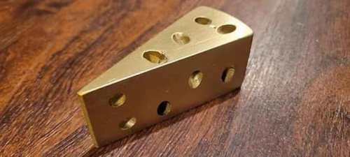 A gold-colored cheese wedge-shaped object with holes, resting on a wooden surface.