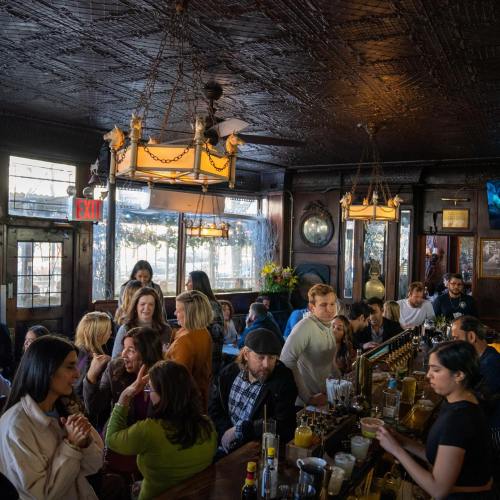 A bustling bar scene with people socializing, drinks on the counter, and warm lighting creating a lively atmosphere.
