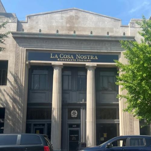Facade of "La Cosa Nostra" Italian restaurant, featuring columns and a clear blue sky above.