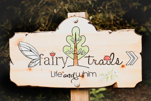 Wooden sign for "Fairy Trails" featuring a tree, leaves, and whimsical designs, with the tagline "Life and Whim."