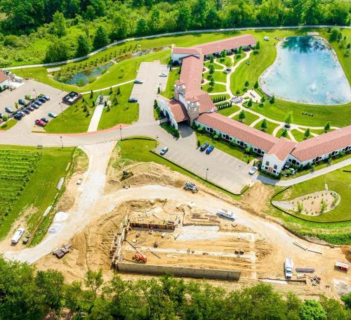 Aerial view of a construction site near a landscaped area with a pond and buildings in the background.
