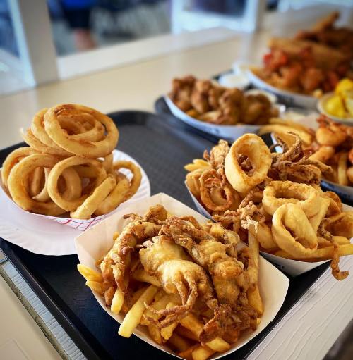 A tray of crispy fried foods, including onion rings and battered seafood served with fries.
