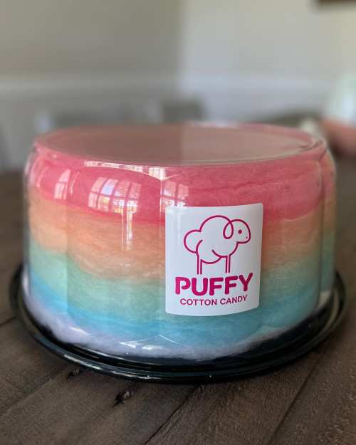A round container of colorful cotton candy with a pink, blue, and white gradient and a "Puffy Cotton Candy" label.