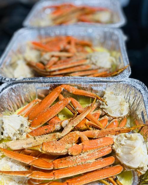 Three trays of steamed crab legs with seasoning and crab meat, arranged neatly in aluminum foil containers.