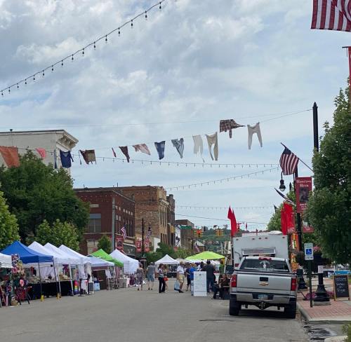 A street lined with vendor tents, hanging laundry, and flags, under a cloudy sky.