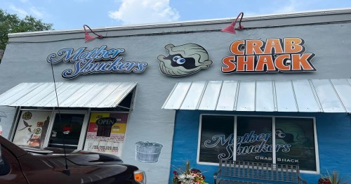 Exterior of a restaurant featuring signs for "Mother Shuckers" and "Crab Shack," with a blue wall and awnings.