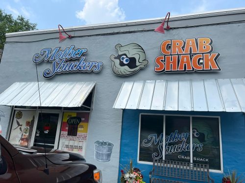 Exterior of a restaurant featuring signs for "Mother Shuckers" and "Crab Shack," with a blue wall and awnings.