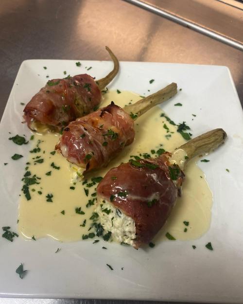 Three prosciutto-wrapped asparagus spears on a white plate, drizzled with sauce and garnished with parsley.