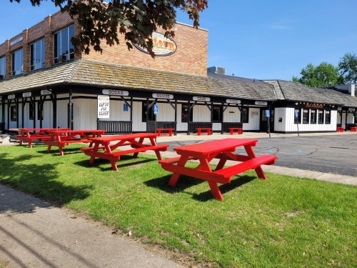 A building with a sloped roof and multiple windows, featuring red picnic tables on a grassy area outside.