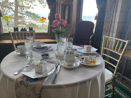 A beautifully set dining table with floral centerpiece, elegant tableware, and a scenic view through large windows.